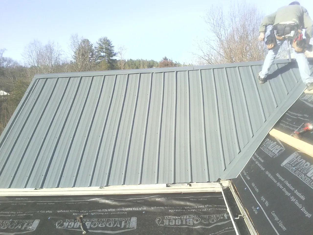 Crew installing dark green standing seam panels over synthetic underlayment in Cuyahoga Falls