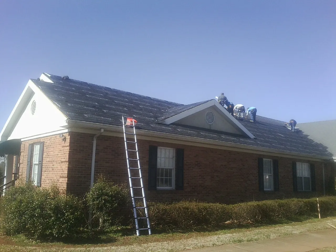 Crew tearing shingles off a brick ranch roof with a ladder set — Emergency Roof Repair work by our crew in Cuyahoga Falls