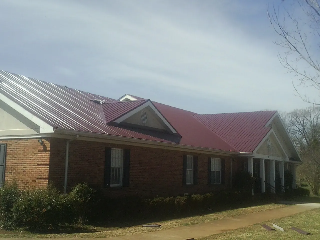 Red metal roof with gabled entries on a long brick building, from a Hail Damage Roof Repair job in Cuyahoga Falls