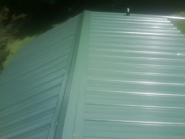 New green metal panels meeting at the ridge of a roof — Flat Roof Repair work by our crew in Cuyahoga Falls