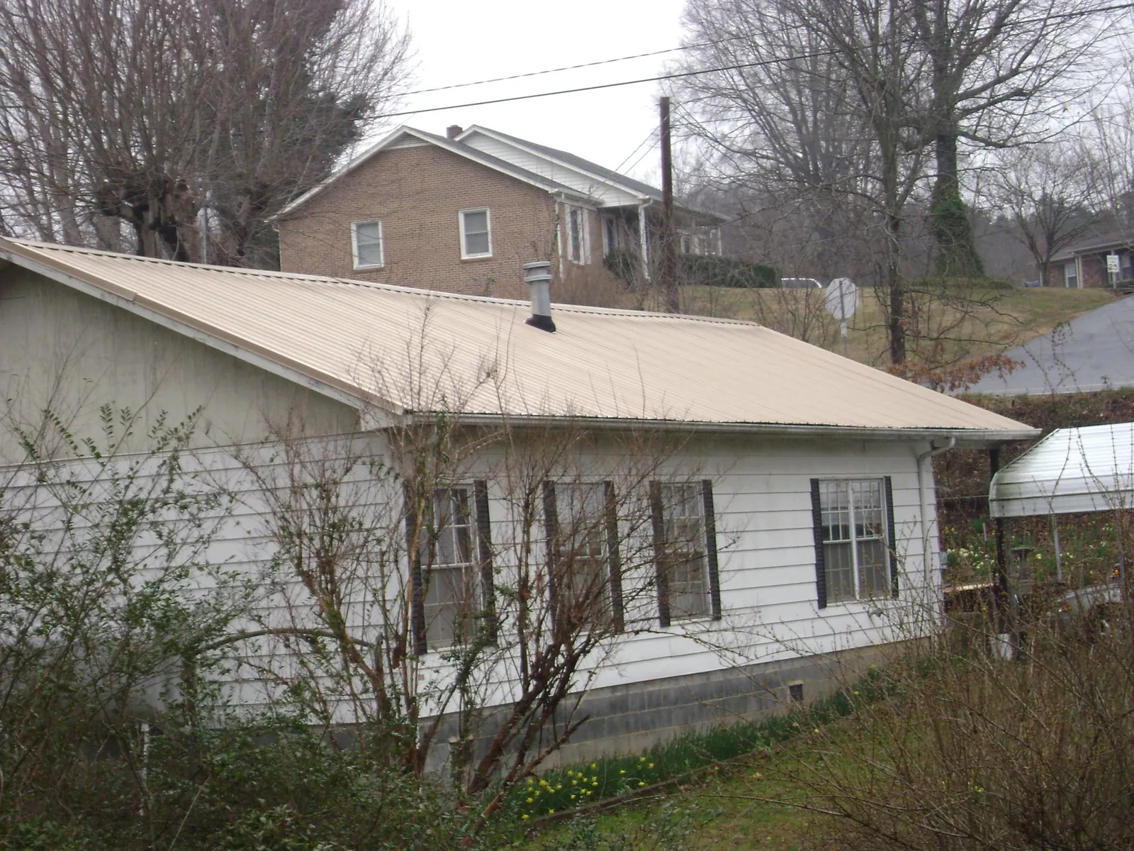 Tan metal roof on a white sided house set into a hillside — Commercial Roofing by Roofing Brothers in Cuyahoga Falls